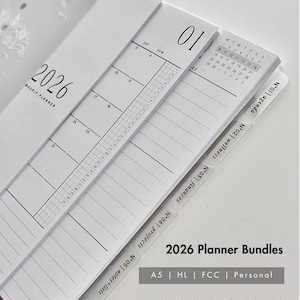 May include: A stack of white 2026 planner bundles with a weekly planner, monthly calendar, and tabbed dividers. The text "2026 Planner Bundles" is visible, along with details about the planner's features, including a personalized etched acrylic dashboard.