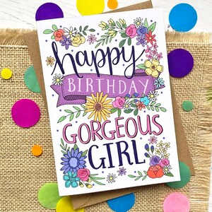 May include: A white card with a floral border and the text "Happy Birthday Gorgeous Girl" in colorful lettering.
