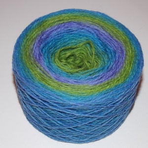 Puede incluir: Un ovillo de lana en tonos azules, verdes y morados. La lana está enrollada en forma de bola y está lista para tejer o hacer ganchillo.