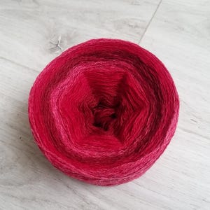 Può includere: Un gomitolo di filato rosso con un gradiente di colore dal rosso scuro al rosa chiaro. Il filato è avvolto in un cerchio ed è pronto per essere utilizzato per la maglia o l'uncinetto.