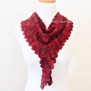 May include: A red crocheted scarf with a scalloped edge and a long, flowing tail. The scarf is displayed on a white mannequin.