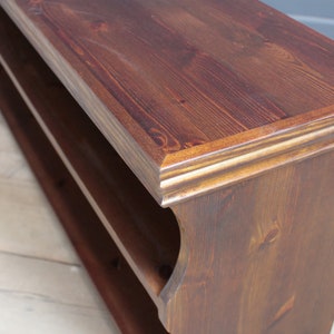 May include: A dark brown wooden shelf unit featuring a rectangular top surface with a decorative molded edge and a single open storage shelf below. The wood grain is visible throughout the piece, showcasing natural knots and a deep stained finish.