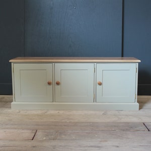 May include: A light green cabinet with three doors and wooden knobs. The cabinet has a wood top and sits on a wooden floor.