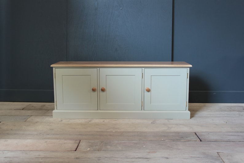 May include: A light green cabinet with three doors and wooden knobs. The cabinet has a wood top and sits on a wooden floor.