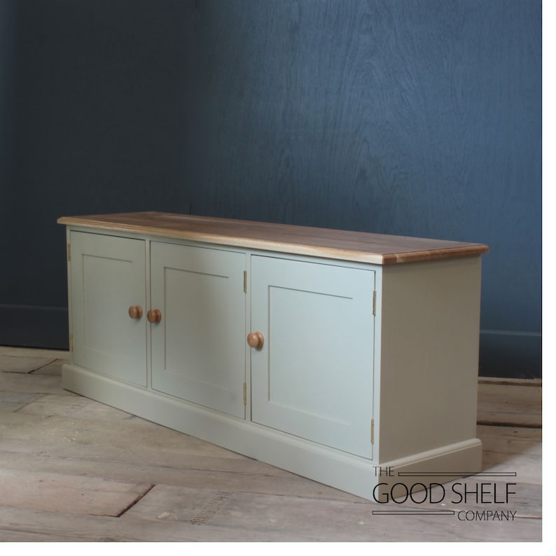 May include: A light green cabinet with three doors and wooden knobs. The cabinet has a wood top and sits on a wooden floor. The text "THE GOOD SHELF COMPANY" is visible on the floor.