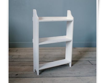 May include: A white wooden shelving unit featuring three horizontal shelves supported by two vertical side panels. The side panels have a curved top edge and a notched base design, providing a stable structure for displaying various items.