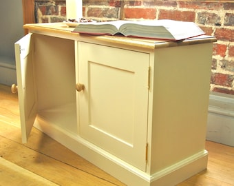 May include: A white cabinet with two doors and a wooden top. The cabinet has a simple design with a single panel on each door and brass hinges. The doors are open, revealing the empty interior of the cabinet.