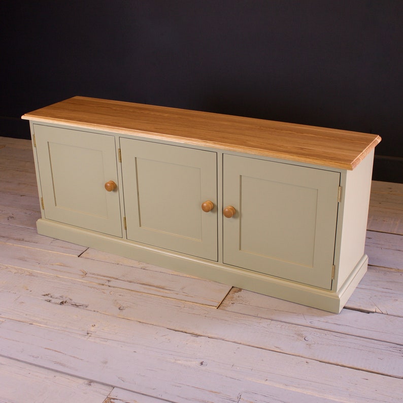 May include: A light green cabinet with three doors and a wood top. The cabinet has a simple design with rounded edges and brass hinges.