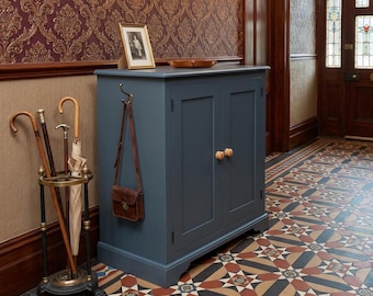 May include: A slate blue cabinet with two doors and light wood knobs, featuring a metal hook on the side holding a brown leather satchel. Next to it stands a black metal umbrella stand containing several walking sticks and a closed beige umbrella.