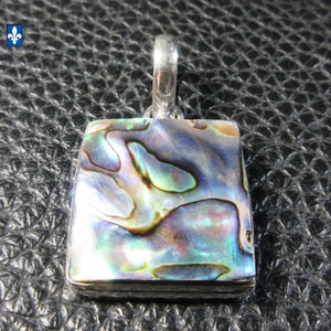 Peut inclure: Pendentif carré orné d'une incrustation de coquillage d'ormeau chatoyant, présentant des reflets irisés bleus, verts et violets. Le pendentif est encadré d'un métal argenté et possède une bélière pour une chaîne. Le coquillage d'ormeau a un motif naturel unique.