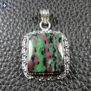 Könnte beinhalten: Silberanhänger mit einem rechteckigen, polierten Stein. Der Stein weist eine Mischung aus grünen, schwarzen und kastanienbraunen Farben auf. Der Anhänger hat einen verzierten Silberrahmen und eine Silberöse für eine Kette.