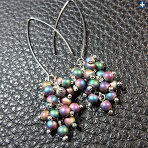 May include: A pair of dangle earrings featuring clusters of iridescent beads in shades of purple, green, and blue. The beads are attached to silver-tone curved ear wires, creating a stylish and eye-catching accessory.