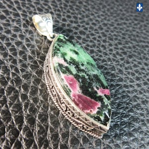 Peut inclure: Un pendentif en argent avec une grande pierre précieuse en forme de goutte d'eau. La pierre présente un mélange de teintes vertes et rouge foncé. Le pendentif a une bordure en argent ornée et détaillée et une bélière décorative.