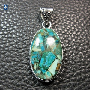 Peut inclure: Pendentif ovale avec une mosaïque de pierres turquoise, bleu sarcelle et crème, sertie dans un cadre en métal argenté. Le pendentif est doté d'une bélière décorative pour une chaîne de collier. La pierre précieuse présente un motif naturel unique.