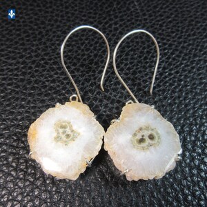 May include: A pair of solar quartz earrings. Each earring features a slice of solar quartz with a white centre and a light brown outer edge. The earrings have silver-coloured ear wires.