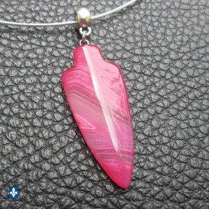 Peut inclure: Un pendentif rose vif en forme de pointe de flèche en pierre polie avec des bandes blanches visibles et des couches translucides. Le pendentif est fixé à une bélière en métal argenté et suspendu à un tour de cou en fil métallique souple.