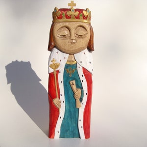 Puede incluir: Una figurita de madera de un rey que lleva una corona roja y dorada, una túnica roja con ribetes blancos y una túnica turquesa debajo. El rey sostiene un rollo en una mano y un cetro en la otra.