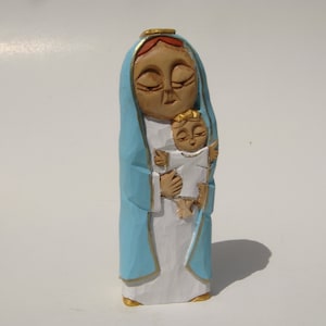 Può includere: Una statuetta in legno intagliata a mano della Vergine Maria che tiene in braccio un bambino Gesù. La statuetta è dipinta in tonalità di blu, bianco e oro.