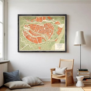 Può includere: Mappa d'epoca incorniciata di Danzica, con una pianta dettagliata della città in tonalità arancioni e verdi. La mappa è racchiusa in una cornice nera e appesa a una parete bianca. La stanza comprende una sedia in legno, cuscini e una lampada da terra.