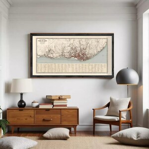 May include: A framed vintage map of Lisbon, Portugal, in a dark wooden frame. The map features detailed city streets and landmarks in red and brown tones, set against a beige background. The map is displayed in a well-lit room with wooden furniture.