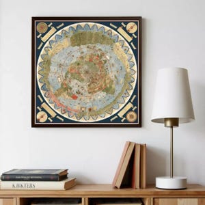 May include: A framed, antique-style map print. The map features a circular design with detailed illustrations and text, set against a blue background. The frame is dark brown. The print is displayed above a wooden shelf with books and a lamp.