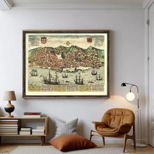 May include: A framed vintage map print depicting a city with detailed streets, buildings, and ships on the water. The map is in shades of brown, green, and beige, with decorative elements and crests. The frame is dark wood.