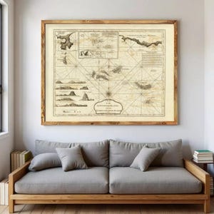 May include: A framed antique map of the Azores Islands, with detailed nautical charts. The map is in a wooden frame and hangs above a grey sofa with cushions. The room has a neutral colour palette.