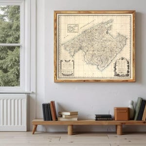 Puede incluir: Un mapa antiguo enmarcado de Mallorca, España, en tonos sepia. El mapa es detallado con características geográficas y texto, enmarcado en un marco de madera rústico. El mapa está colgado en una pared blanca.