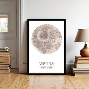 May include: Framed print featuring a detailed map of Vienna, Austria, in a circular design. The city name and coordinates are printed below the map. The print is in a black frame and displayed on a wooden floor.