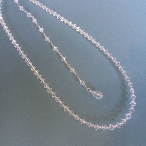 May include: A delicate crystal necklace with a teardrop pendant. The necklace is made of small, faceted crystals and is strung on a silver chain.