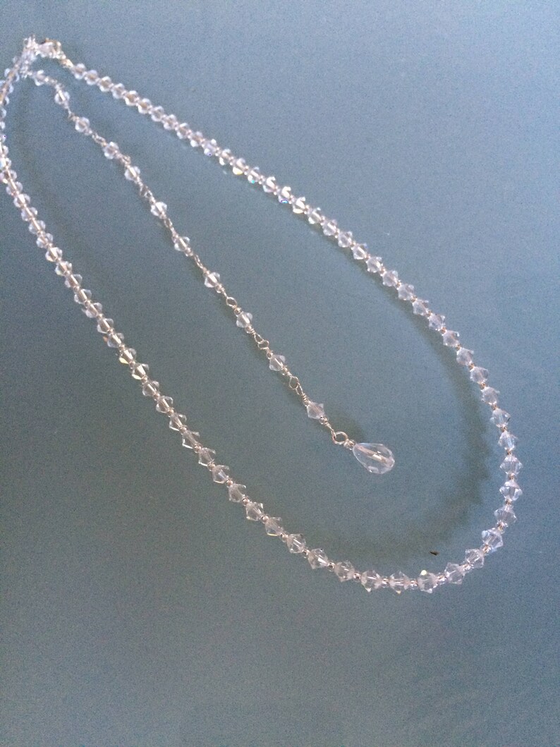 May include: A delicate crystal necklace with a teardrop pendant. The necklace is made of small, faceted crystals and is strung on a silver chain.