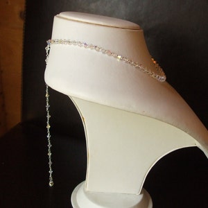 May include: A white crystal necklace with a long, dangling strand of crystals. The necklace is displayed on a white mannequin bust.