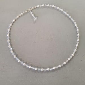 May include: A necklace composed of small white pearls and clear crystals, secured with a silver clasp. A small crystal pendant hangs from the clasp. This necklace is suitable for formal events or casual wear.