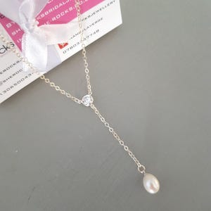 May include: A delicate silver-toned lariat necklace featuring a fine chain, a single round clear cubic zirconia stone set in a bezel, and a small white teardrop-shaped pearl pendant hanging at the end of the vertical drop section of the chain.