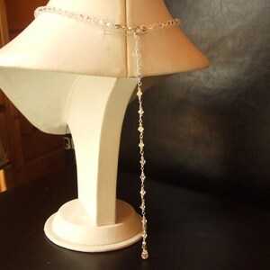 May include: A long, delicate crystal necklace with a silver clasp. The necklace is displayed on a white mannequin bust.