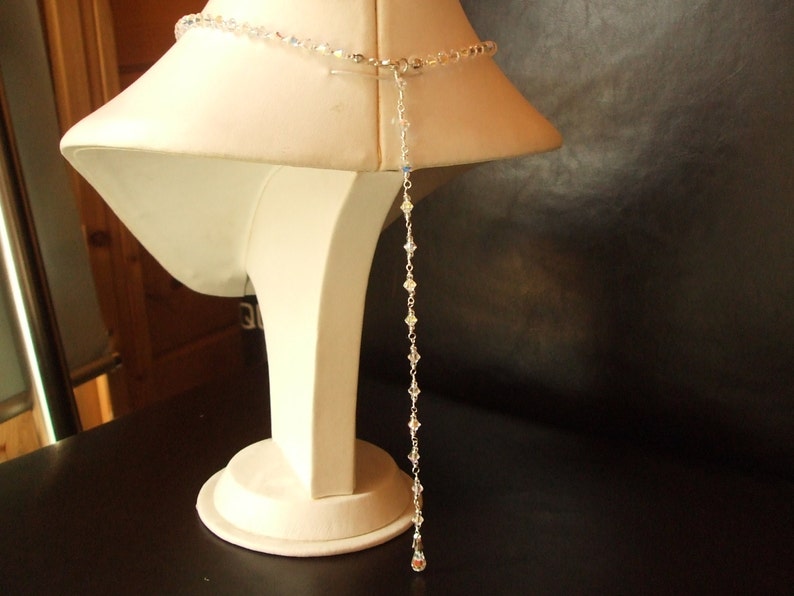 May include: A long, delicate crystal necklace with a silver clasp. The necklace is displayed on a white mannequin bust.