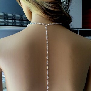 May include: A delicate crystal back necklace with a teardrop pendant. The necklace is made of small, clear crystals strung on a silver chain.