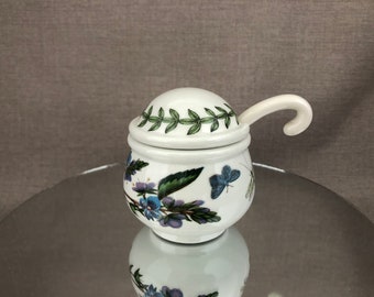 May include: White ceramic sugar bowl with a lid and a spoon. The bowl has a floral design with green leaves, blue flowers, and a butterfly.