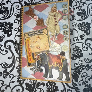May include: A scrapbook page with a circus theme. The page features a red, white, and blue checkered background with a gold glitter arrow pointing to the number 62. There is a vintage circus poster for Barnum & Bailey's Greatest Show on Earth, a picture of a clown, and a picture of an elephant. The text "BIG TOP" is written in large letters on the right side of the page.