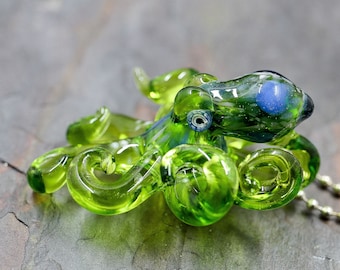 May include: A green glass octopus pendant with blue eyes, hanging from a silver chain. The octopus is detailed with textured glass and has a realistic shape.