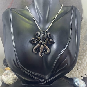 May include: A silver chain necklace with a black glass octopus pendant. The octopus has a dark gray body and silver tentacles.