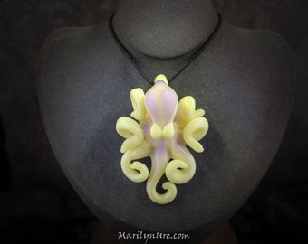 May include: A glass octopus pendant with a light purple body and yellow tentacles. The pendant is hanging from a black cord on a grey mannequin.