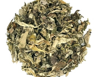 May include: A circular pile of dried loose leaf tea consisting of various shades of green, brown, and pale yellow. The mixture features fragmented, curled, and crinkled leaves with visible stems and small botanical pieces throughout the cluster.