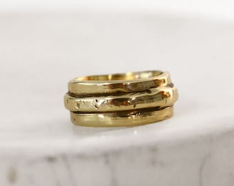 May include: A gold-toned metal ring featuring a multi-band design with a textured, uneven surface. The ring consists of three distinct, stacked-looking bands that are joined together, creating a layered appearance with a polished, reflective finish.