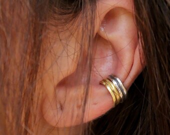 May include: A multi-layered ear cuff featuring two distinct bands, one in a polished gold tone and one in a textured silver tone, positioned securely on the middle section of the outer ear cartilage, creating a stacked appearance on the ear.