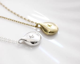 May include: Two necklaces with teardrop-shaped pendants, one in gold and one in silver. Each pendant features a small, stamped letter K on the front surface. The pendants are attached to delicate, matching metal chains that extend out of frame.