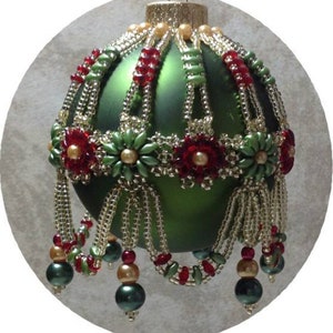 Könnte beinhalten: Ein grüner gläserner Weihnachtsbaumschmuck, der mit roten und goldenen Perlen verziert ist. Der Schmuck hat einen Perlenbesatz und eine goldene Spitze.