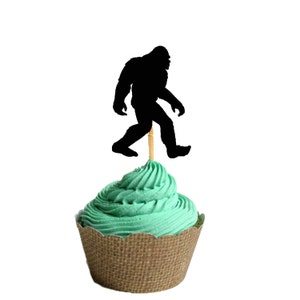 May include: A green cupcake with a brown burlap cupcake liner topped with a black silhouette of a Bigfoot walking on a toothpick.