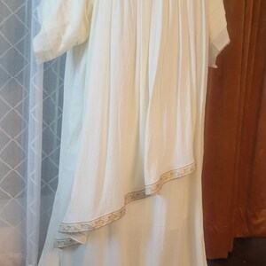 Puede incluir: Un vestido blanco fluido con un ribete decorativo alrededor del escote y el dobladillo. El vestido tiene un corte holgado y c&oacute;modo y es perfecto para una variedad de ocasiones.
