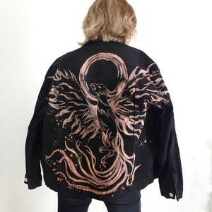 May include: A black denim jacket with a bleached phoenix design on the back. The phoenix is a mythical bird that symbolizes rebirth and renewal.